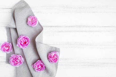Beautiful pink rose flowers on gray linen fabric tablecloth. Decorative side frame on white vintage wooden table. Home table decoration concept. Flat lay, top view, space for your textの写真素材