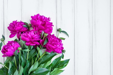 Bunch of beautiful pink peony flowers on white vintage wooden table. Wedding, gift card or any holiday background. Flat lay, top view with place for textの写真素材