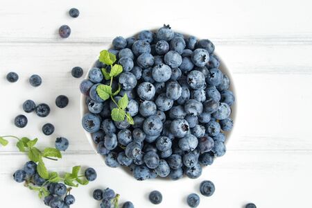 Fresh blueberries with mint branches in white bawl on white wooden table. Flat lay, top viewの写真素材