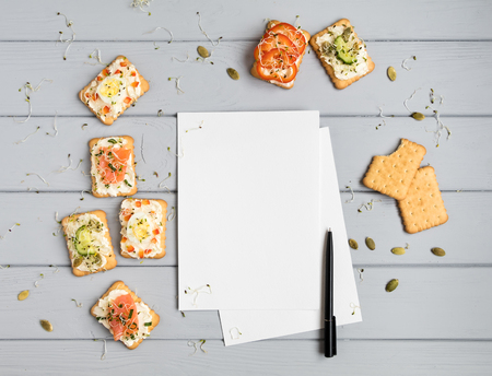 Recipe book page and tasty crackers with cream cheese, sweet pepper, salmon, eggs, cucumbers, seeds, micro greens. Appetizers on grey table with a blank page. Top view, flat layの写真素材
