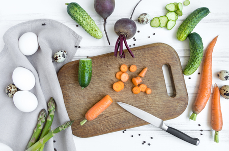 Sliced carrots and a knife on wooden cutting board, surrounded with vegetables and eggs. Home cooking concept. Salad or any vegetarian dish. Flat lay, top viewの写真素材