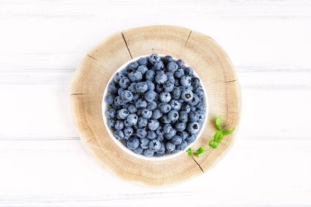Fresh blueberries with mint branches in white bawl on white wooden table. Flat lay, top viewの写真素材