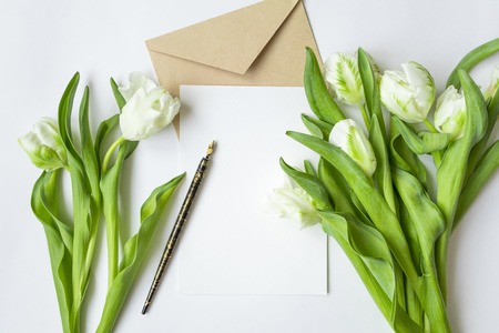 Letter, envelope and fresh bouquet on white background. Wedding invitation cards or love letter with white tulips. Romantic or holiday concept, top view, flat lay, overhead viewの写真素材