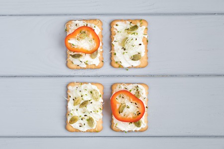 Tasty square crackers with cream cheese, sweet pepper, pumpkin seeds and micro greens. Appetizers on...