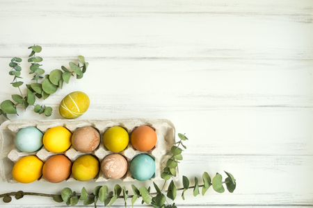 Easter eggs colored with colorful natural paints in an egg tray on white wooden tableの写真素材