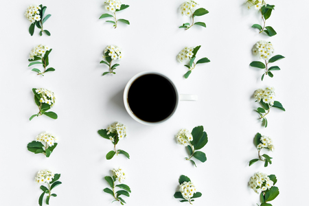 Cup of black coffee and beautiful white flowering Spirea arguta (brides plant) branches pattern on white table. Flat lay, top view. Romantic patternの写真素材