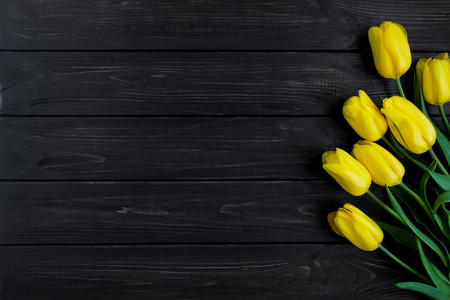 Beautiful bouquet of yellow tulips in corner of dark vintage wooden table. Holiday border, home decor concept. Top view, flat layの写真素材