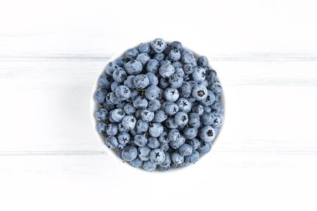 Fresh blueberries in white bawl on white wooden table. Minimalistic flat lay composition, top viewの写真素材