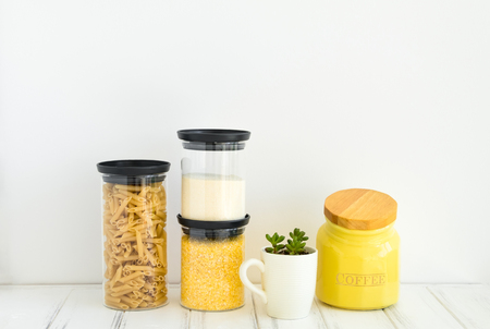 Pasta, coffee and cereals in glass jars and a small plant in a cup on white background. Organized home kitchen and healthy eating concept. Minimalist bright composition with place for textの写真素材