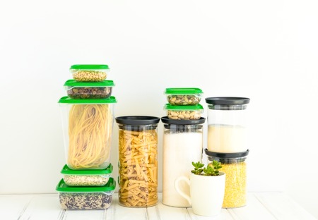 Pasta and cereals in glass jars and plastic boxes, a small plant in a cup on white background. Organized home kitchen and healthy eating concept. Minimalist bright composition with place for textの写真素材