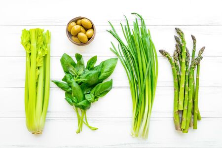 Green fresh herbs and vegetables on white wooden background. Flat lay, eco vegan background with celery, basil leaves, onions, olives and asparagus. View from aboveの写真素材