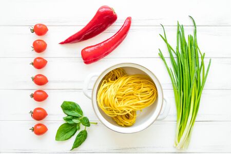 Ingredients for healthy Italian pasta with herbs and vegetables or salad, bright background. Pasta nests in a pan, onions, tomatos, sweet pepper, basil leaves. Flat lay, view from aboveの写真素材