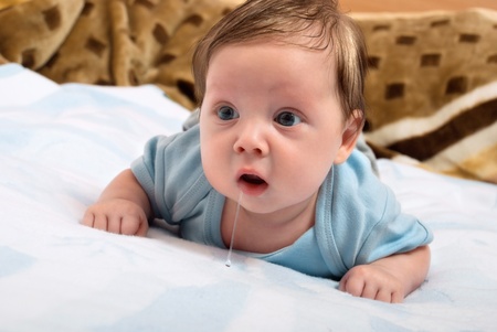 Cute little baby looks into the camera and drooling while lying on the bed. Creative concept photosの写真素材