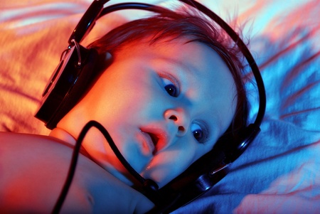 The small baby listening to music with headphones on tinted background.の写真素材