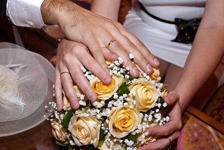 Wedding bouquet from white and pastel yellow roses, hands and rings.