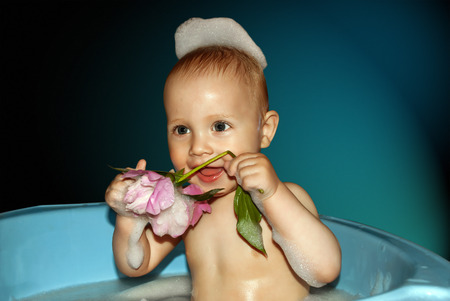Little boy in bath with flower in hand on blue background.の写真素材