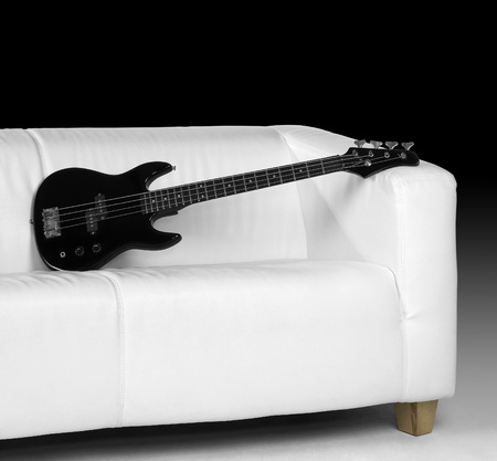 black bass guitar on white couch in dark backの写真素材