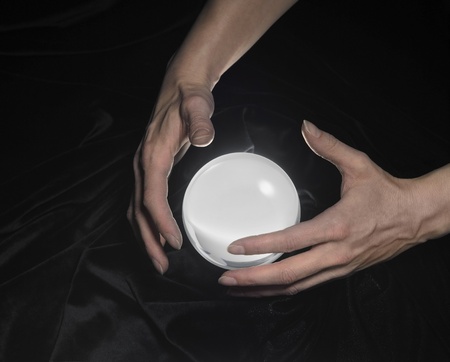 high angle shot of a glowing crystal ball surrounded by black crinkly fabrics and two hands aroundの写真素材