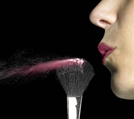 studio shot of a female mouth while blowing on powdered make-up brush in black back