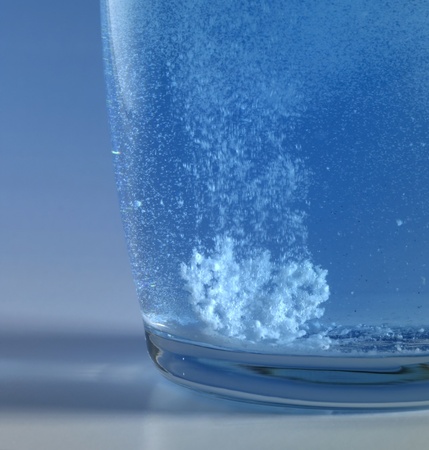 dissolving fizzy tablet floating in a glass of water. Studio photography in blue backの写真素材