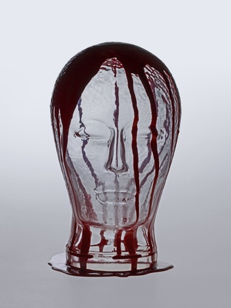 generic human "dummy" head made of glass, overwhelmed with red fluid in light grey backの写真素材