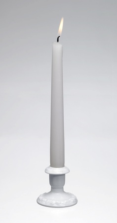 Studio shot of a a white burning candle and a white porcelain candle holder in light backの写真素材