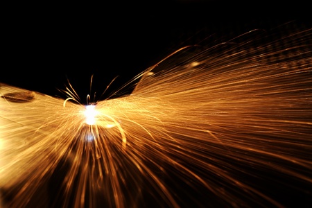industrial theme showing a laser cutting machine at work, in dark back with lots of glowing sparks