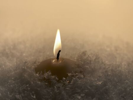 closeup of a burning yellow candle in artificial snowの写真素材