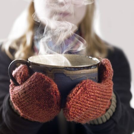 detail of a woman with woolen gloves holding a hot steaming cupの写真素材