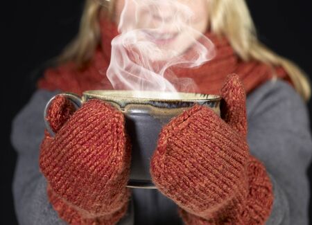 detail of a woman with woolen gloves holding a hot steaming cupの写真素材