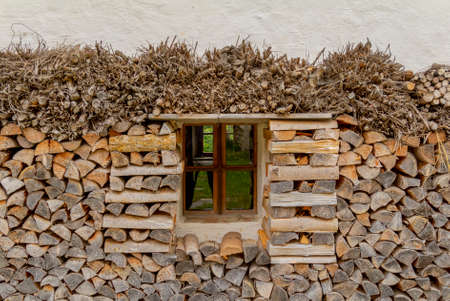house facade including a small window surrounded by firewood