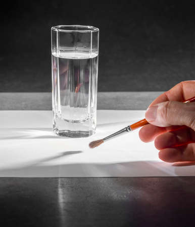 Art and craft theme showing a painting hand with paintbrush on white paper sheet including a glass...