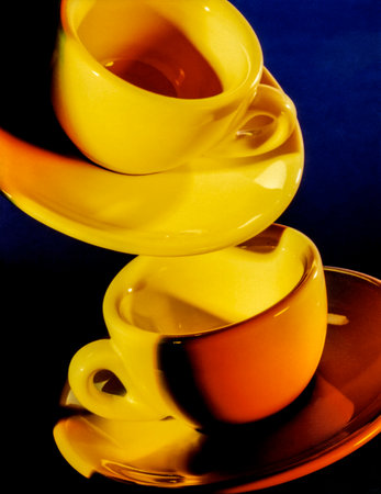 Brightly illuminated yellow cups with saucer in dark blue backの写真素材
