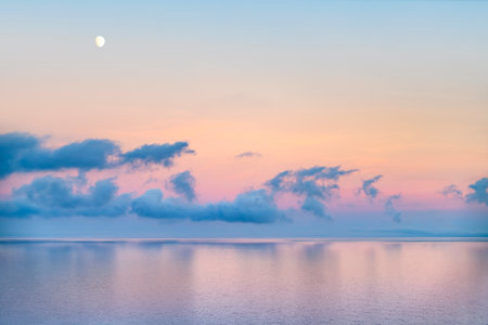 Ocean scenery including some clouds and the moon at evening time