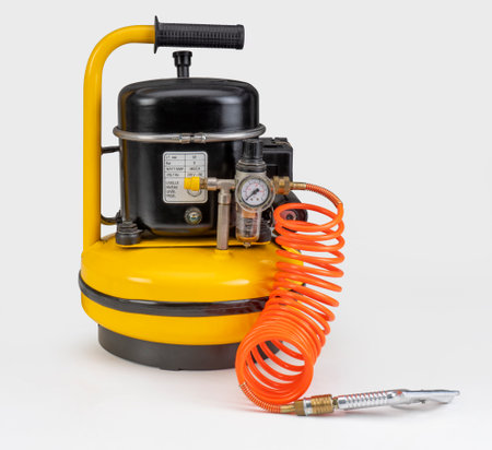 Yellow air compressor with orange tube in white backの写真素材