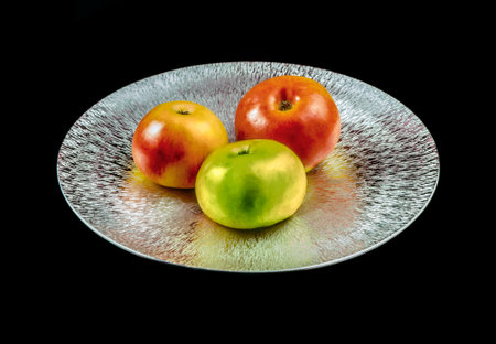 Three apples on a reflective textured metal plate isolated in black backの写真素材