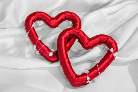 Two heart shapes made of red fabrics on white textile ground