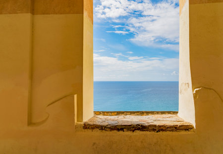 Sunny Mediterranean sea scenery seen through a window opening in a historic wall lake in Liguria, Italyの写真素材