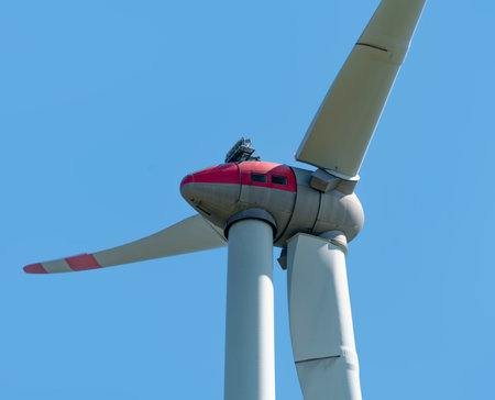 Low angle closeup shot of a sunny illuminated wind turbine nacelle in front of blue skyの写真素材