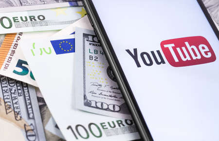 dollars, euro banknotes and YouTube logo on the screen smartphone. YouTube is a free video sharing application that anyone can watch. Moscow, Russia - March 15, 2019のeditorial素材