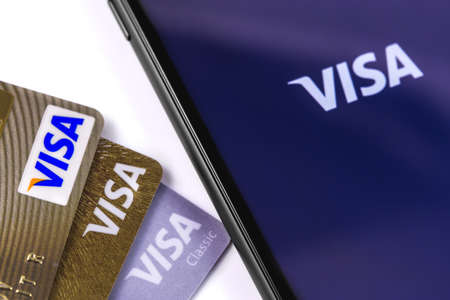 Visa credit card and smartphone with Visa logo on the screen. Visa - American multinational company providing services of payment operations. Moscow, Russia - March 12, 2019のeditorial素材