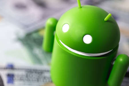 closeup Google Android figure standing on money, dollars. Google Android is the operating system for smartphones, tablet computers, e-books, game consoles, and other devices. Moscow, Russia - March 17, 2019のeditorial素材