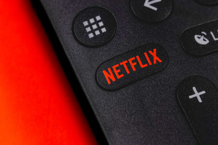 Netflix button on the remote controller on red background. Netflix is an international leading...
