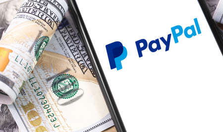 PayPal logo on the screen smartphone, and money, dollars. Paypal is an internet based digital money...
