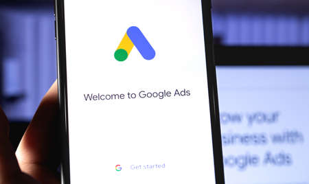 Google Ads mobile app on the screen smartphone with notebook background closeup. Ads is a service of...