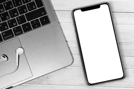 iPhone mockup and Apple Macbook with Earpods closeup at the white office desk. Blank screen mobile...
