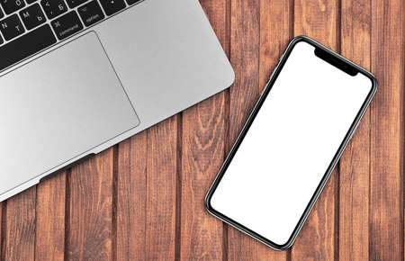iPhone mockup with Macbook closeup at the wooden desk. Blank screen mobile phone for graphic display montage. Moscow, Russia - December 26, 2019のeditorial素材