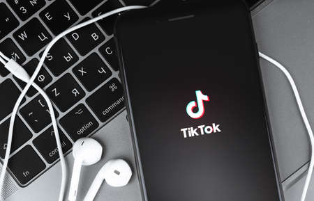 TikTok logo on the sceen smartphone and Earpods closeup on notebook background. TikTok is app to...