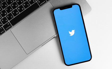 Twitter mobile app logo on screen smartphone iPhone, with Macbook notebook. Twitter is a social media online service for microblogging and networking communication. Moscow, Russia - January 12, 2021のeditorial素材