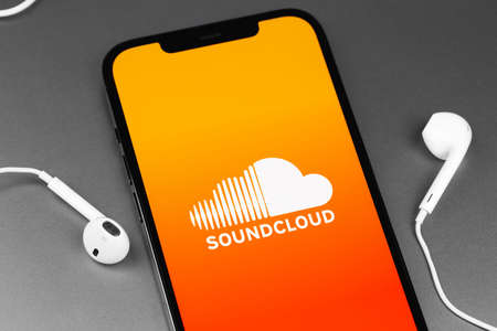 Soundcloud logo mobile app on screen smartphone iPhone with EarPods headphones. SoundCloud is a global online audio distribution platform. Moscow, Russia - March 11, 2021のeditorial素材